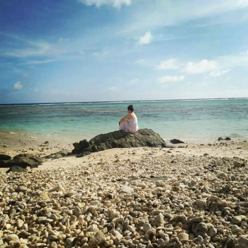 Person sitting on a rock on a beach with ocean and heaven above