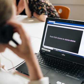 a person holds a headphone to his ear and is looking at a laptop on a table